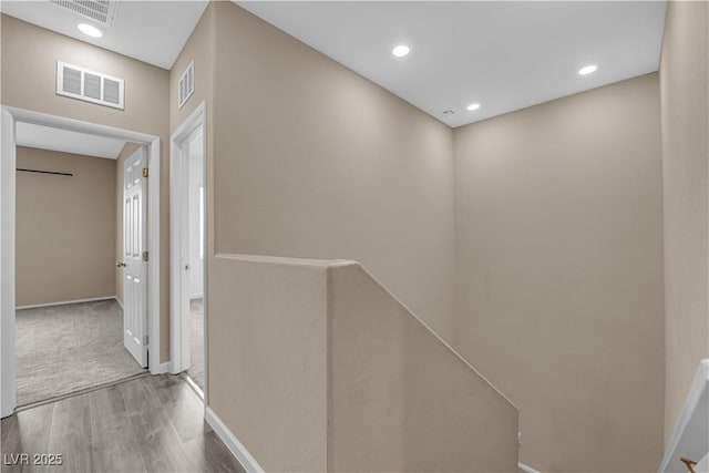 corridor with visible vents, an upstairs landing, and wood finished floors