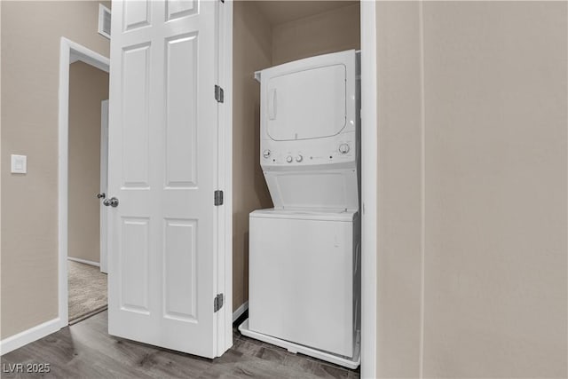 clothes washing area with stacked washer and dryer, laundry area, wood finished floors, visible vents, and baseboards