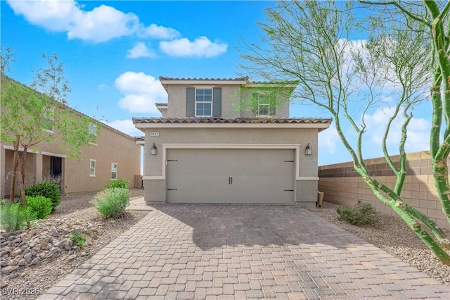 mediterranean / spanish-style home featuring an attached garage, fence, decorative driveway, and stucco siding