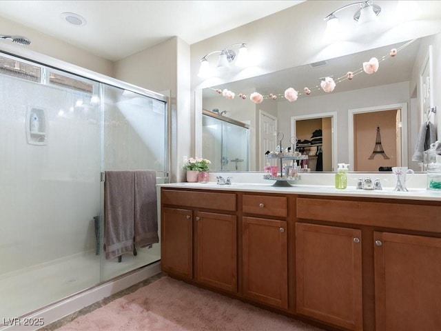 full bath featuring double vanity, a sink, a shower stall, and a spacious closet