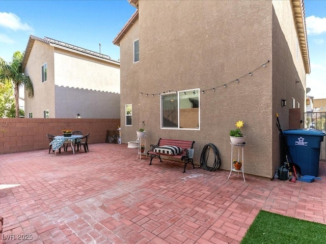 rear view of house with a patio area, fence, and stucco siding