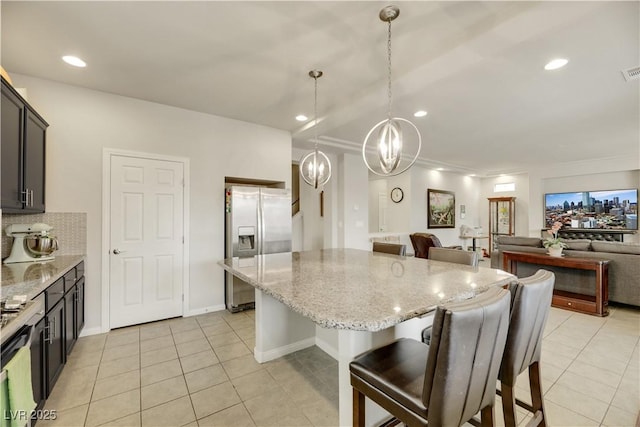 kitchen with light tile patterned flooring, a breakfast bar, a kitchen island, stainless steel fridge with ice dispenser, and light stone countertops