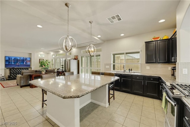 kitchen with visible vents, backsplash, appliances with stainless steel finishes, light stone countertops, and a kitchen bar