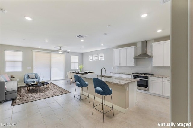 kitchen with wall oven, wall chimney exhaust hood, a breakfast bar, open floor plan, and a sink