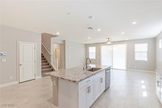 kitchen featuring dishwasher, an island with sink, light stone counters, white cabinetry, and a sink