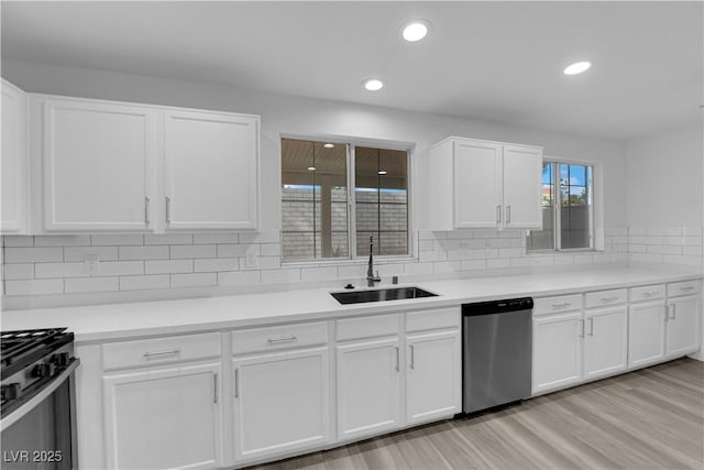 kitchen featuring range with gas cooktop, white cabinets, dishwasher, and a sink