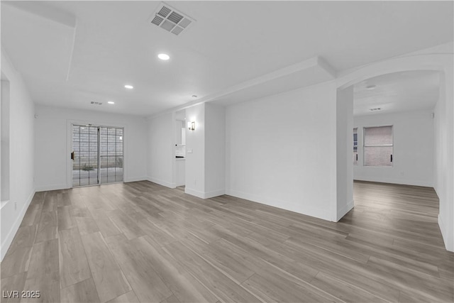 empty room with light wood finished floors, baseboards, visible vents, arched walkways, and recessed lighting