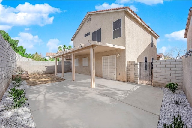 back of house with stucco siding, a gate, a patio area, a fenced backyard, and a tiled roof