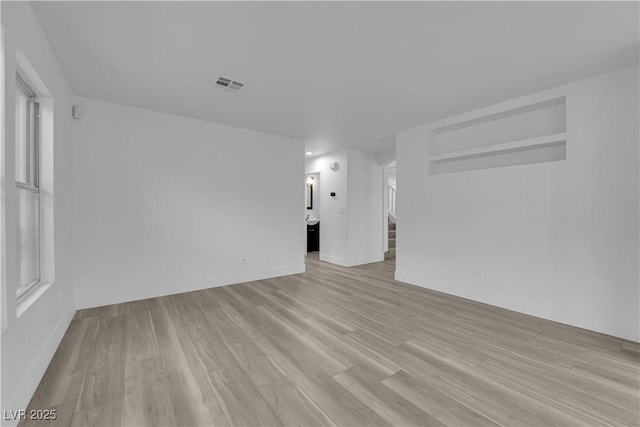 empty room featuring light wood-type flooring, visible vents, baseboards, and stairs