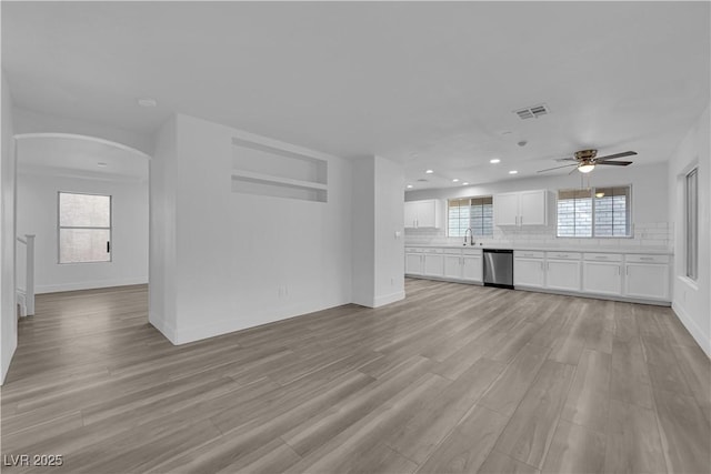 unfurnished living room with light wood finished floors, baseboards, visible vents, arched walkways, and recessed lighting