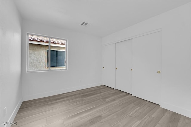 unfurnished bedroom featuring light wood finished floors, a closet, visible vents, and baseboards