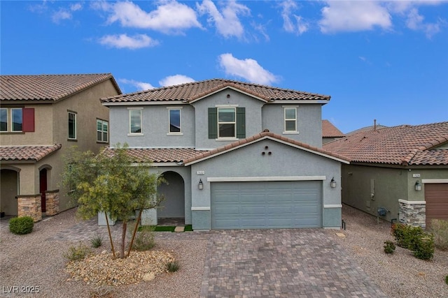 mediterranean / spanish-style house featuring an attached garage, a tile roof, decorative driveway, and stucco siding