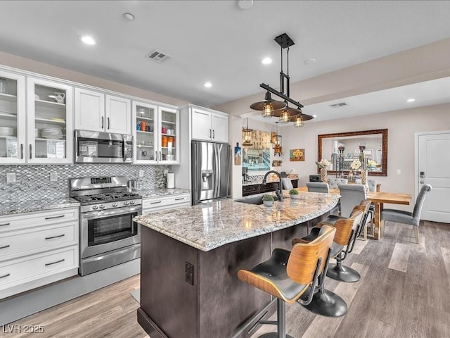 kitchen featuring light stone countertops, visible vents, a sink, appliances with stainless steel finishes, and a kitchen breakfast bar