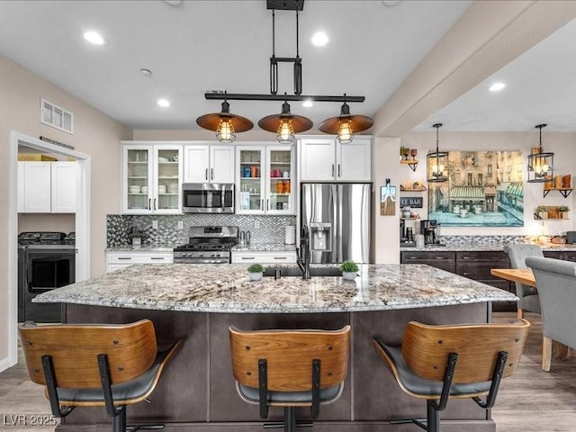 kitchen with visible vents, a breakfast bar, appliances with stainless steel finishes, white cabinets, and decorative backsplash