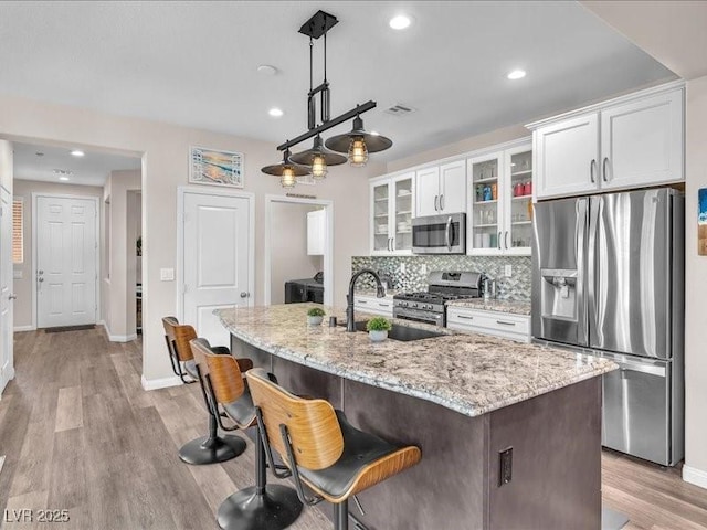 kitchen featuring light wood-style flooring, tasteful backsplash, white cabinetry, appliances with stainless steel finishes, and light stone countertops