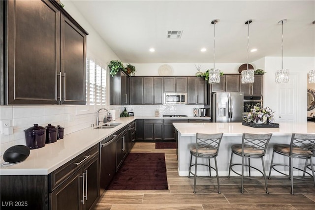 kitchen with dark brown cabinets, appliances with stainless steel finishes, a breakfast bar, and a sink