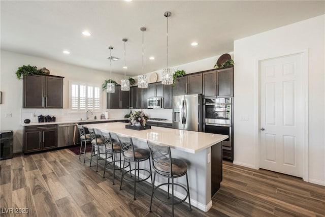 kitchen featuring dark wood-style floors, appliances with stainless steel finishes, a kitchen island, and dark brown cabinetry