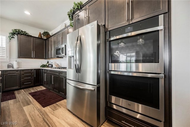 kitchen featuring light countertops, backsplash, appliances with stainless steel finishes, dark brown cabinetry, and wood finished floors