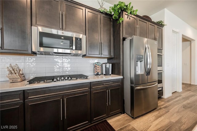 kitchen featuring dark brown cabinetry, decorative backsplash, appliances with stainless steel finishes, light countertops, and light wood-type flooring