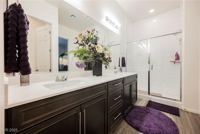 bathroom featuring double vanity, a stall shower, visible vents, wood finished floors, and a sink