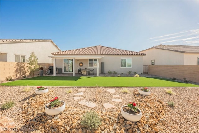 rear view of property with a fenced backyard, a tile roof, a yard, stucco siding, and a patio area