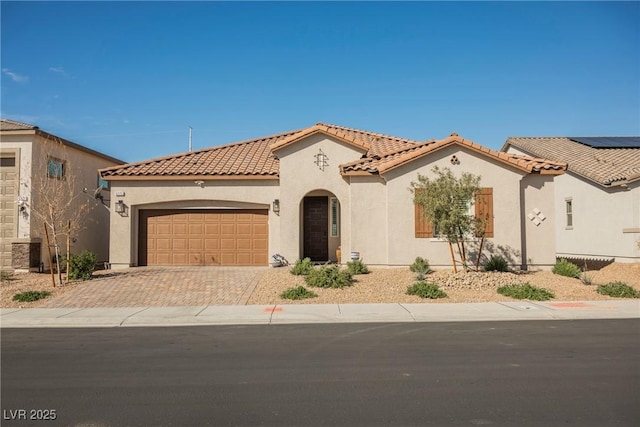 mediterranean / spanish-style home featuring a tiled roof, decorative driveway, an attached garage, and stucco siding