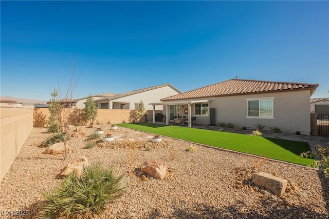 rear view of property featuring a fenced backyard, a lawn, a tile roof, and stucco siding