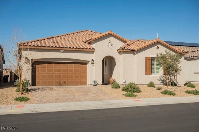 mediterranean / spanish home featuring a garage, a tile roof, decorative driveway, roof mounted solar panels, and stucco siding