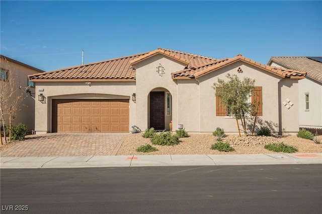 mediterranean / spanish-style home with decorative driveway, an attached garage, a tile roof, and stucco siding