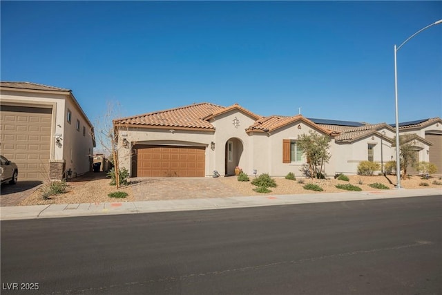 mediterranean / spanish-style home featuring driveway, a tiled roof, an attached garage, roof mounted solar panels, and stucco siding