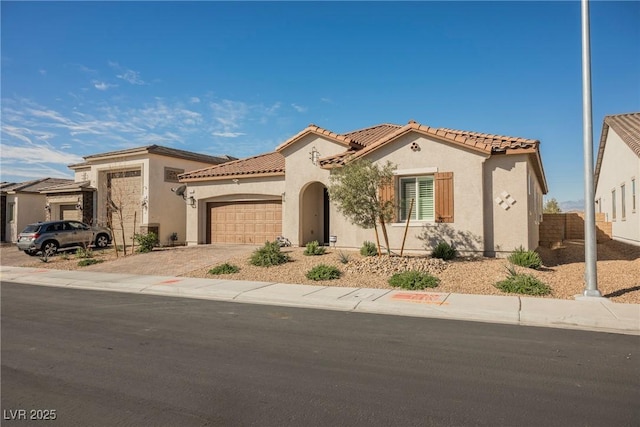 mediterranean / spanish home featuring a garage, driveway, a tiled roof, and stucco siding