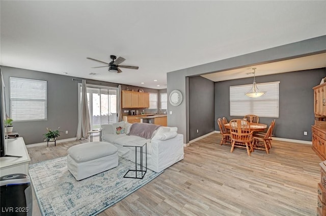 living area featuring light wood finished floors, ceiling fan, and baseboards