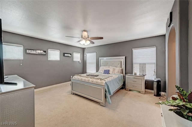 bedroom featuring light carpet, a textured ceiling, arched walkways, and baseboards