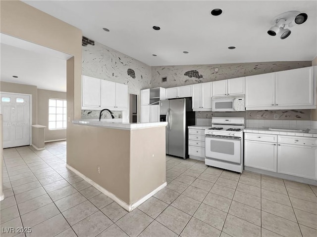 kitchen with tile countertops, light tile patterned floors, white appliances, white cabinetry, and vaulted ceiling