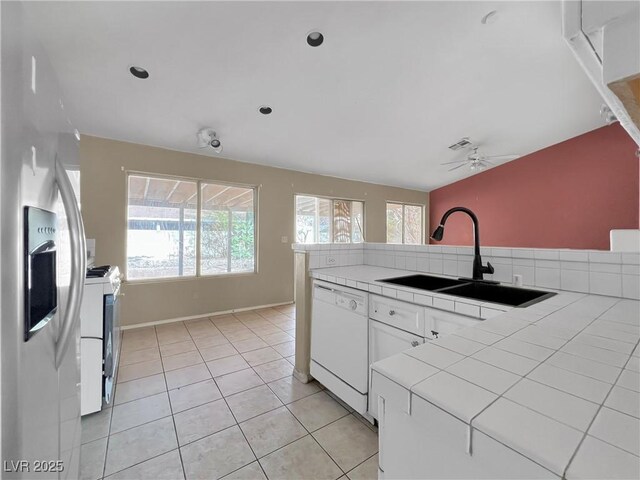 kitchen featuring white appliances, light tile patterned floors, tile counters, vaulted ceiling, and a sink