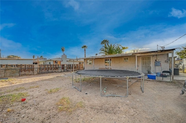 back of house featuring a trampoline and fence