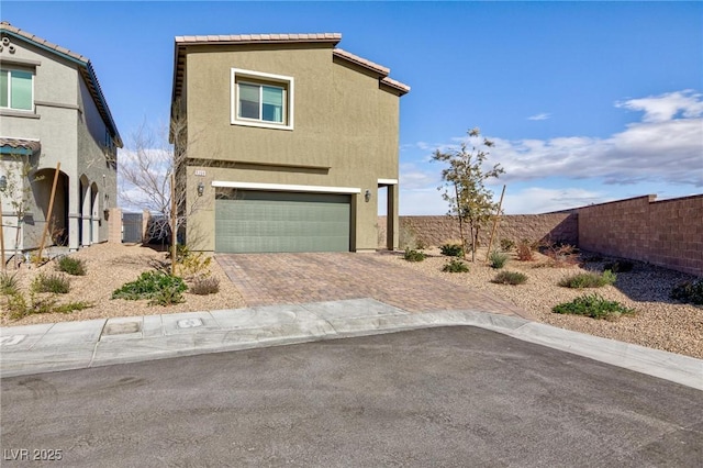 view of front of house featuring an attached garage, fence, decorative driveway, and stucco siding