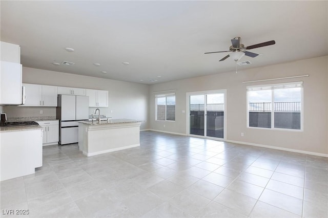 kitchen with freestanding refrigerator, open floor plan, white cabinetry, an island with sink, and baseboards