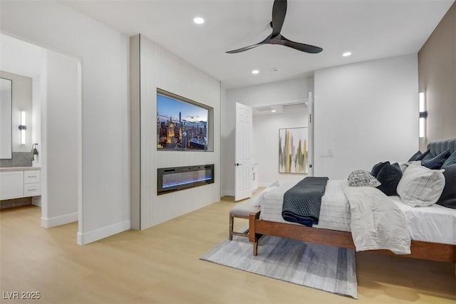 bedroom with light wood finished floors, recessed lighting, ensuite bathroom, and a glass covered fireplace