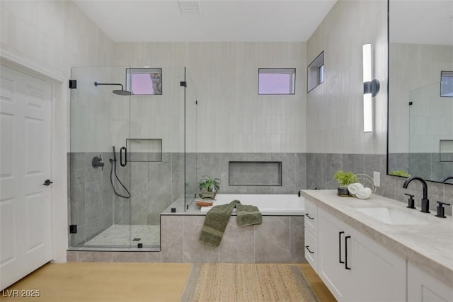 bathroom with a bath, a shower stall, visible vents, and tile walls