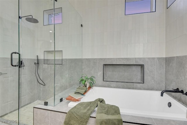 bathroom featuring a stall shower, a garden tub, and tile walls