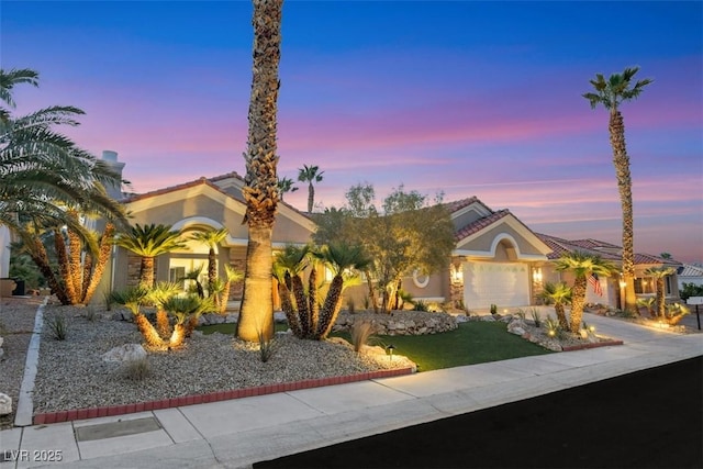 view of front facade with a tile roof, driveway, an attached garage, and stucco siding