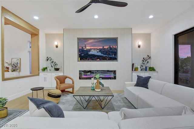 living room featuring baseboards, a ceiling fan, a glass covered fireplace, wood finished floors, and recessed lighting