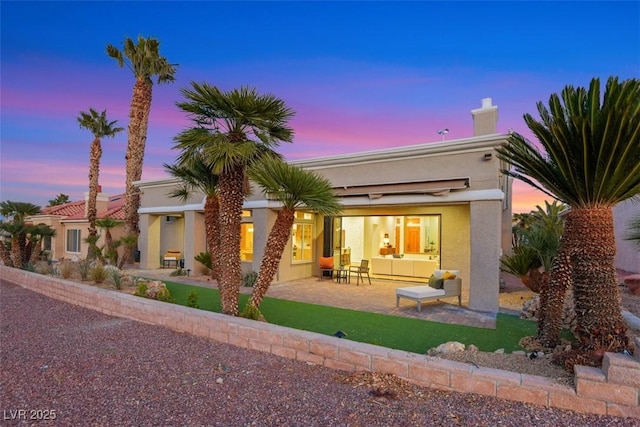 back of property at dusk featuring a chimney, a patio area, outdoor lounge area, and stucco siding