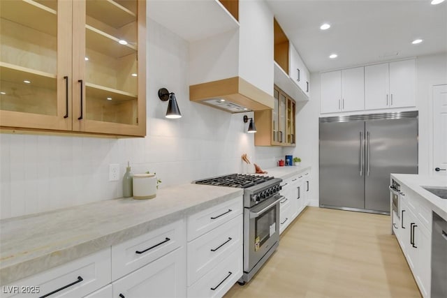 kitchen featuring high end appliances, decorative backsplash, glass insert cabinets, light stone counters, and custom exhaust hood