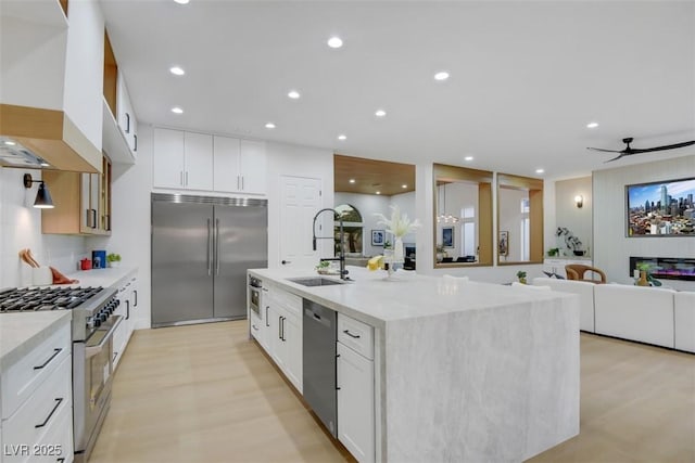 kitchen featuring high quality appliances, a kitchen island with sink, premium range hood, a sink, and recessed lighting