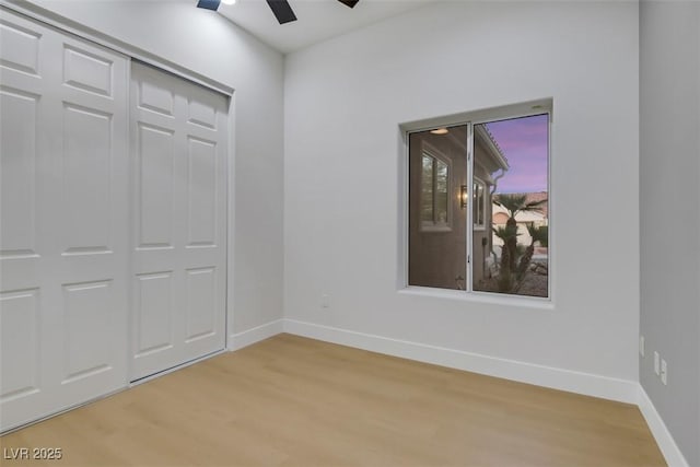 unfurnished bedroom featuring light wood finished floors, ceiling fan, baseboards, and a closet