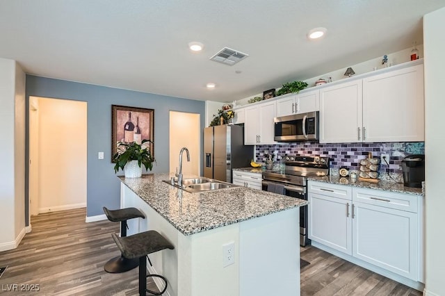 kitchen with stainless steel appliances, wood finished floors, a sink, visible vents, and decorative backsplash