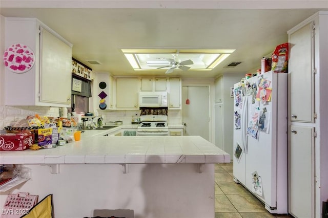 kitchen featuring white appliances, decorative backsplash, tile countertops, a peninsula, and light tile patterned flooring