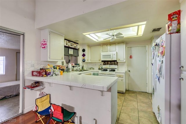 kitchen with tasteful backsplash, white appliances, a peninsula, and light tile patterned floors